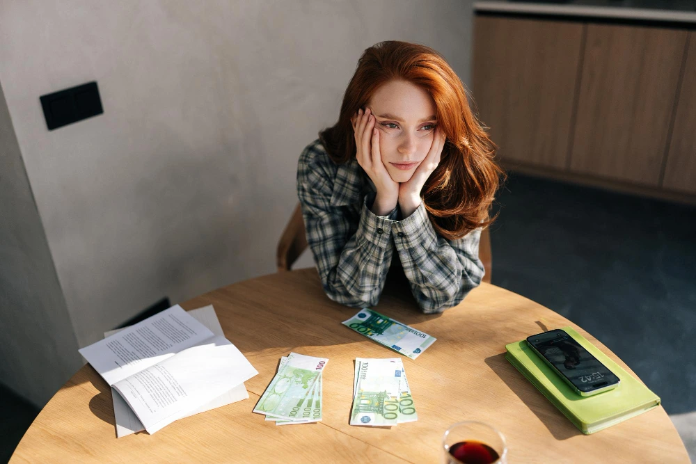 estoy desesperada encesito dinero urgente: mujer preocupada sentada ante billetes, móvil y documentos sobre la mesa