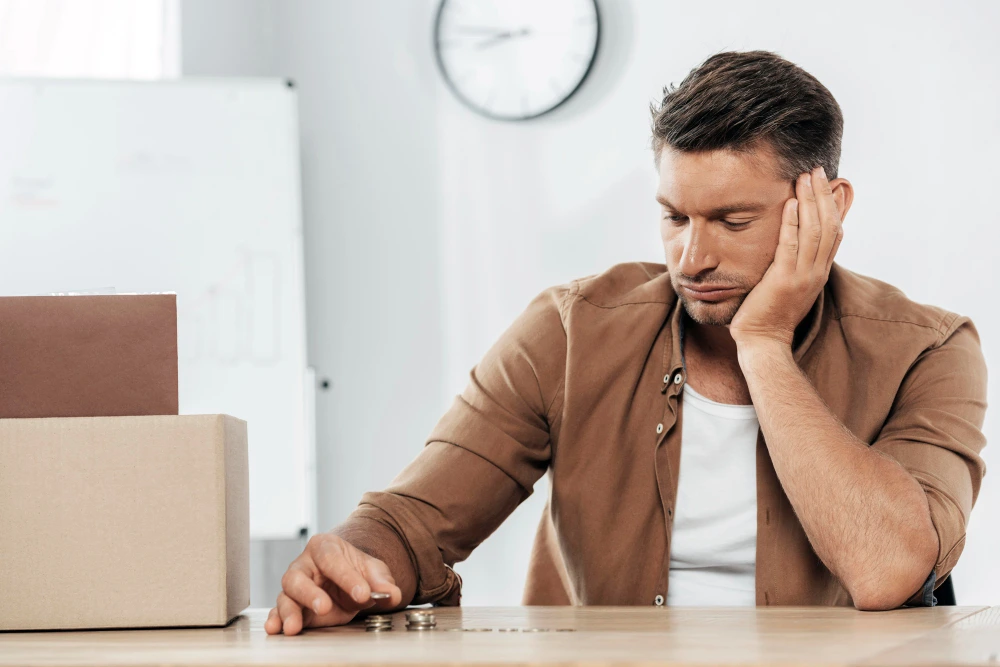 Hombre con expresión de preocupación mirando unas monedas sobre la mesa, simbolizando la frase necesito dinero para pagar deudas y pago como sea.