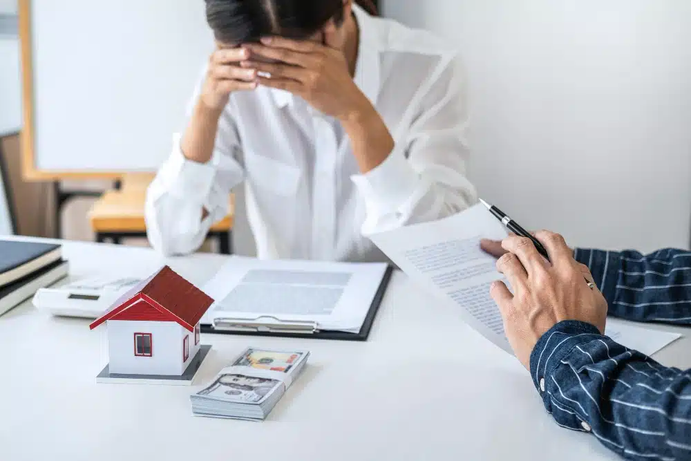 Muer en escritorio con una casa, dinero y con el préstamo hipotecario que se enfrenta a la noticia de una ejecución hipotecaria con vivienda habitual, mientras que otra persona le informa de que hay alternativas como la oposición a la ejecución hipotecaria con vivienda habitual