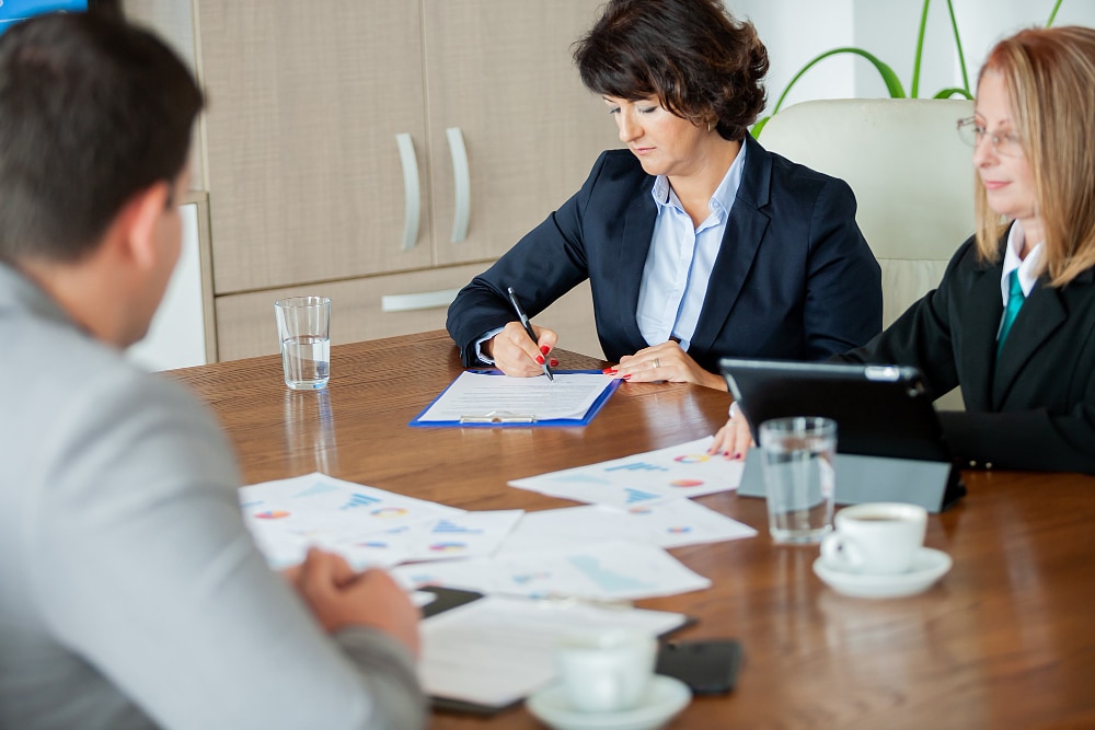 Pareja de mujeres emprendedoras en el banco firmando contratos frente a un trabajador del banco en relación a los préstamos ico autónomos del covid19 para conseguir la nulidad del aval ico