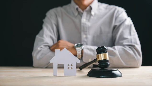 Un mazo de juez junto a una pequeña casa de madera blanca, simbolizando la protección de la vivienda para el deudor de buena fe de la ley segunda oportunidad con Asoban Abogados.