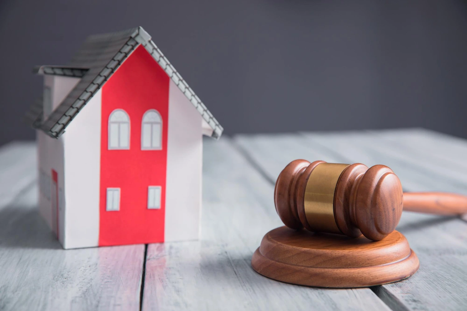 Maqueta de una vivienda junto a un mazo de juez sobre una mesa de madera, ilustrando como parar una subasta judicial.