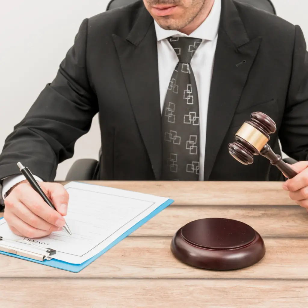 Abogado de traje firmando un documento legal junto a un mazo de madera, representando una subasta judicial inmuebles.