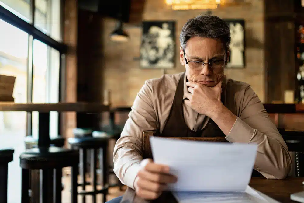 Joven preocupado revisando un documento de deuda en una cafetería - prescripción de deudas y plazos legales.