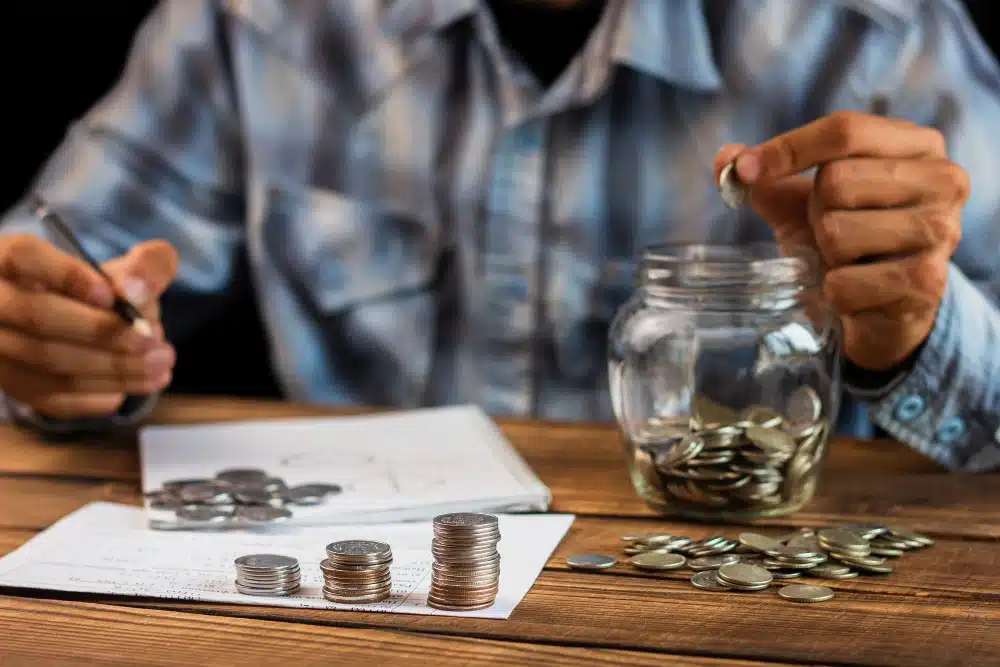 Hombre contando monedas sobre la mesa mientras revisa documentos, representando cómo calcular cuándo prescribe la deuda fondo buitre, acumulación de intereses y pagos atrasados.