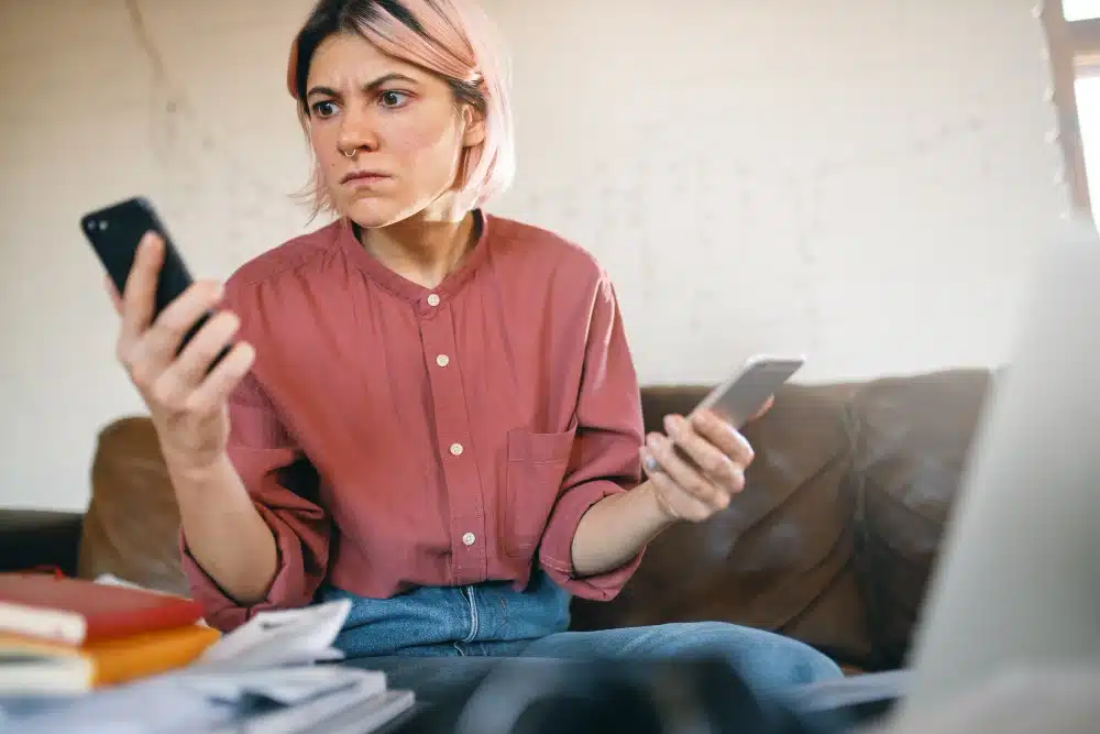 Mujer preocupada revisando dos teléfonos móviles, reflejando la confusión y estrés causados por estafas y ataques de phishing en Instagram