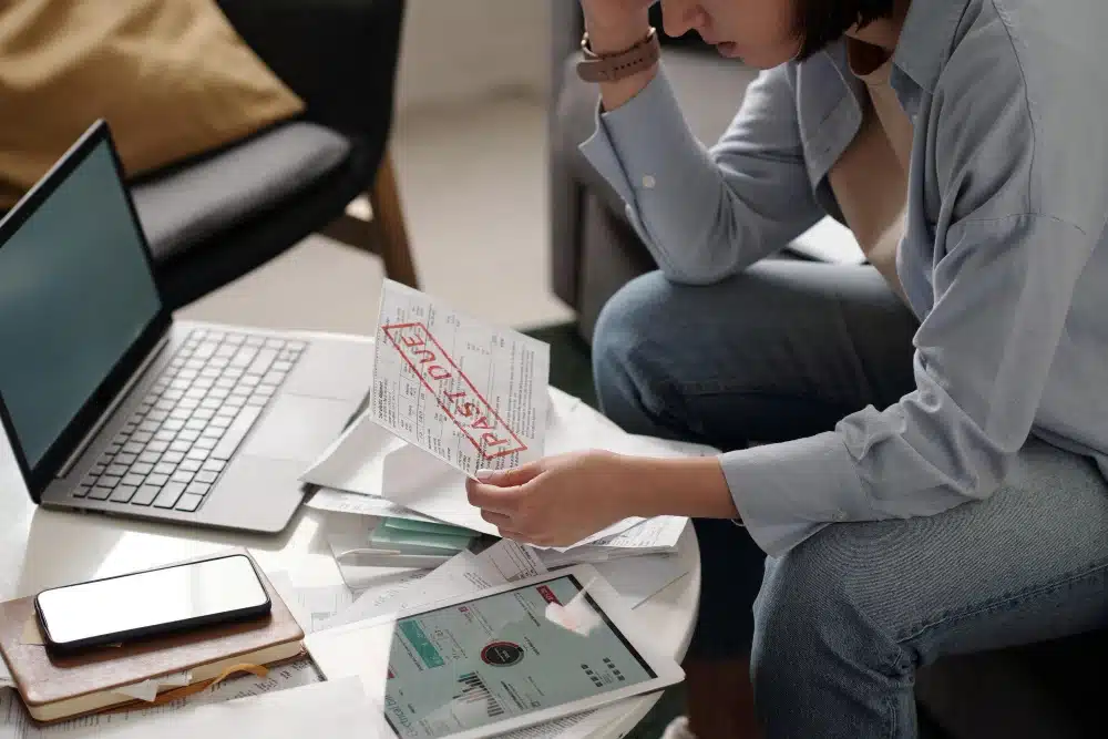 Mujer revisando facturas y documentos con la marca 'past due', relacionada con la consulta sobre cómo verificar si estás en una lista de morosos