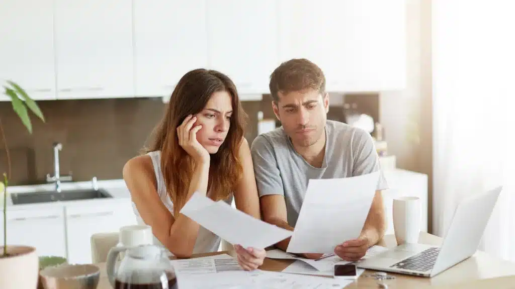 Pareja preocupada revisando documentos y facturas en casa, simbolizando los efectos del índice IRPH en sus hipotecas de su vivienda protegida.