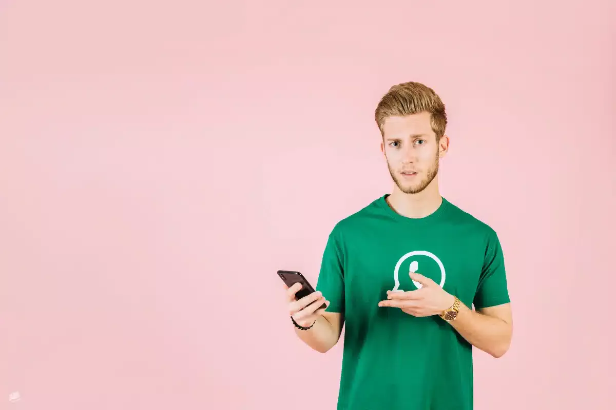 Hombre joven con camiseta verde y logo de WhatsApp, sosteniendo un teléfono con expresión de duda – qué pasa si abro un WhatsApp desconocido según Asoban Abogados.