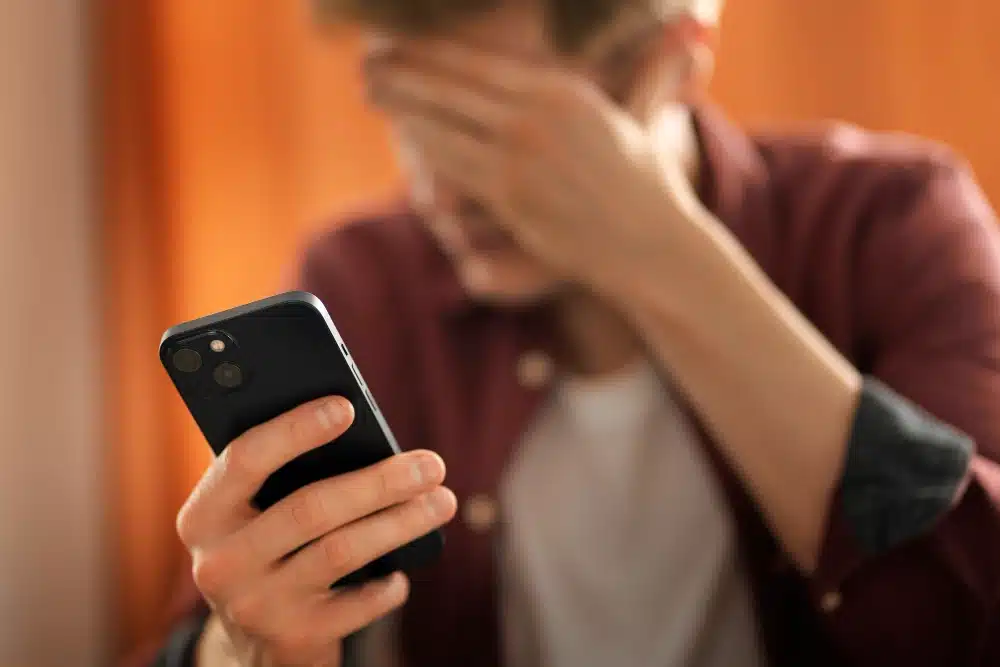 persona con una mano en la frente y delante de su móvil que se pregunta qué hacer si me amenaza un proxeneta por Whatsapp y preocupado por haber caído en la estafa sicarios whatsApp