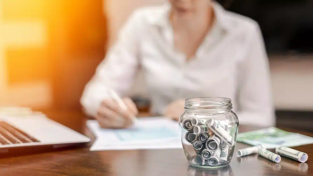 Mujer revisando documentación junto a un tarro con billetes enrollados como símbolo del plan de pagos en la Ley de la Segunda Oportunidad.
