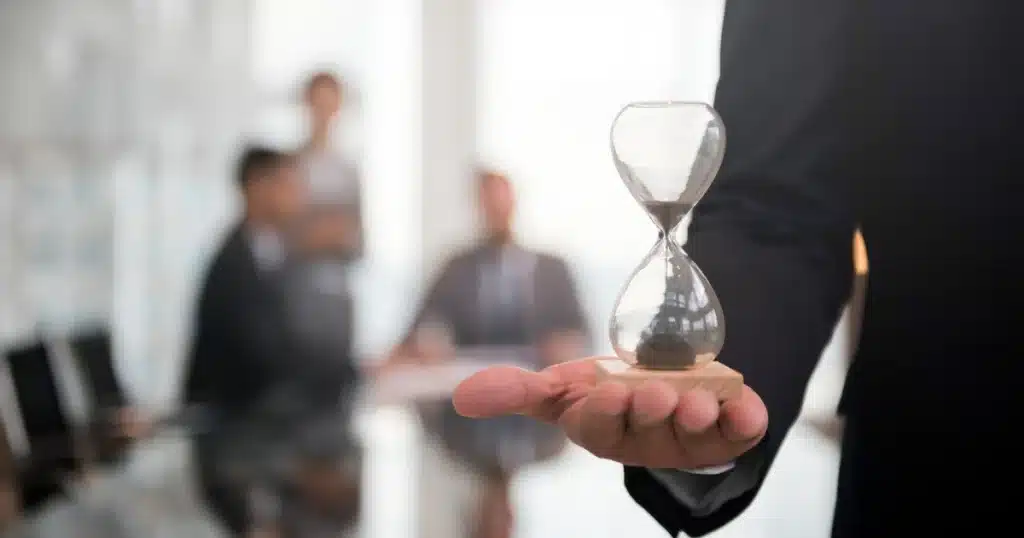 Primer plano de un reloj de arena sostenido por una persona con traje, representando el tiempo límite antes de un posible desahucio por impago de alquiler.