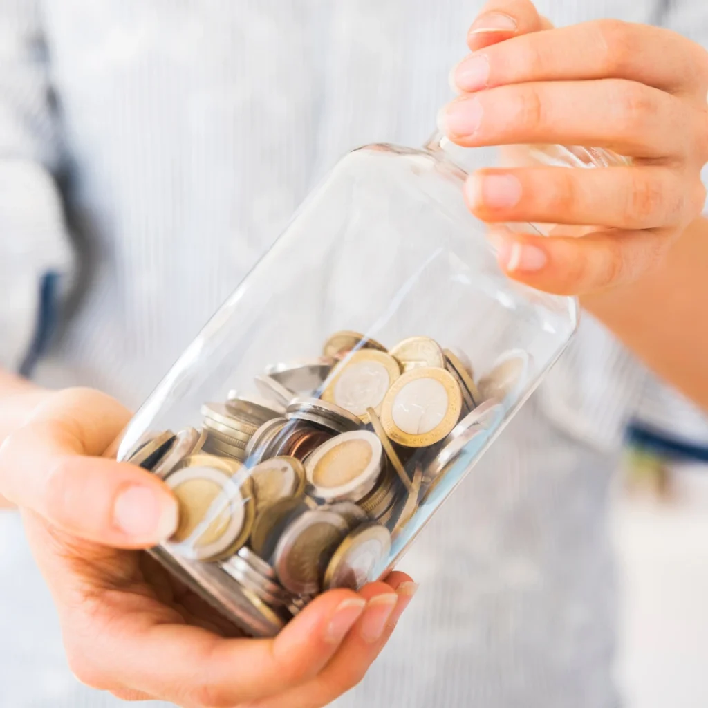 Persona sosteniendo un frasco de vidrio lleno de monedas, representando el impacto económico cuando Fidinda incurre en usura.