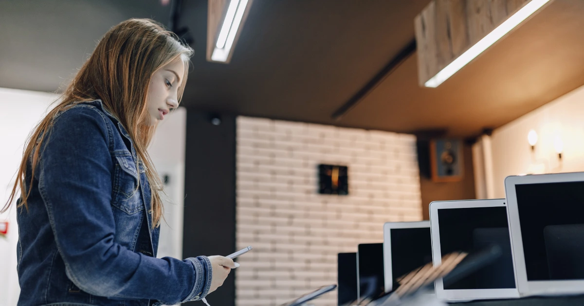 Joven consultando su informe CIRBE en una tienda de tecnología con varios ordenadores en exhibición.