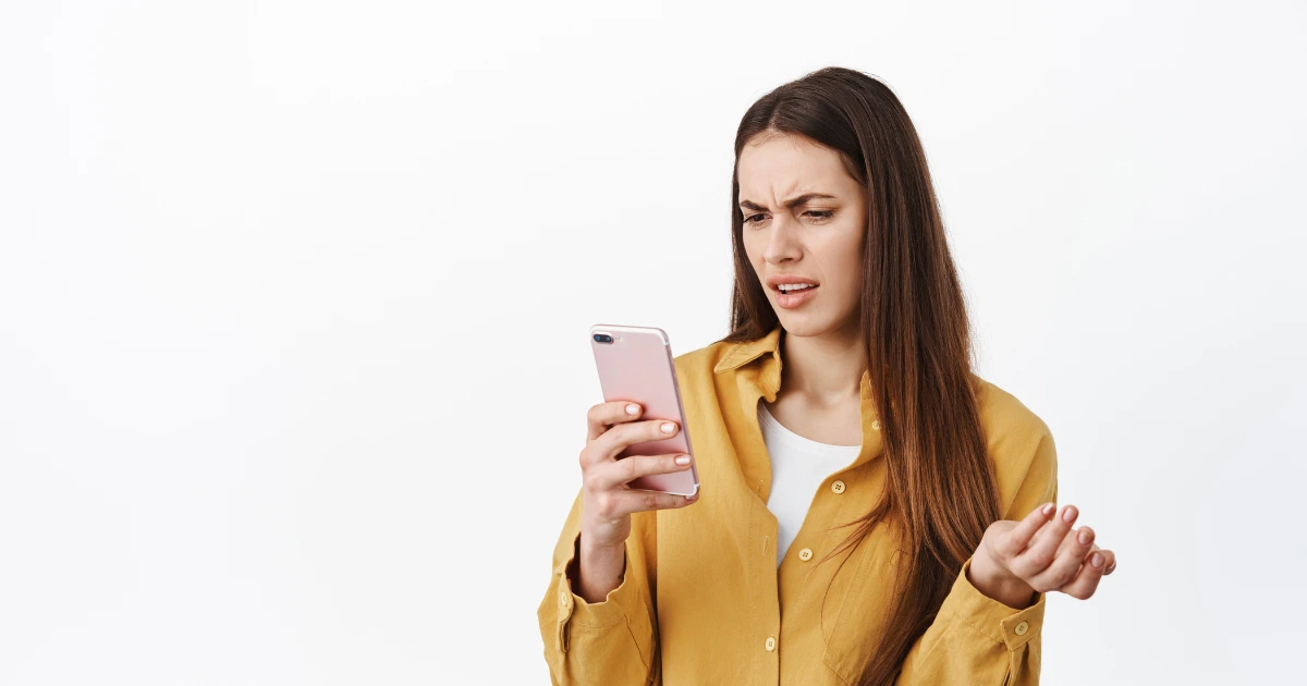 Mujer confundida mirando su móvil, expresión de duda al preguntarse cómo saber si estoy siendo estafado por internet o por mensajes sospechosos.