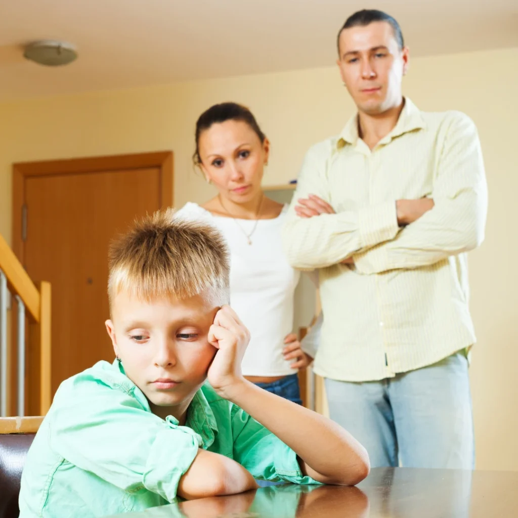 Niño triste en casa con sus padres preocupados, ilustrando la preocupación por los ingresos de una familia vulnerable.