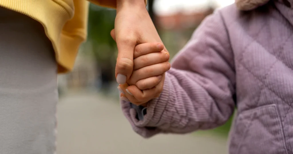 Mano de persona adulta sosteniendo la mano de una niña, simbolizando apoyo a persona vulnerable económicamente.