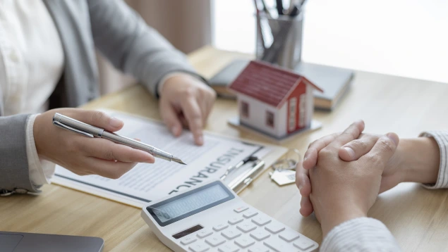 Asesor financiero orienta a un cliente sobre las condiciones de su hipoteca IRPH, con documentos, calculadora y una maqueta de casa sobre la mesa, en un contexto de afectados IRPH que buscan reclamar por cláusulas abusivas y falta de transparencia.