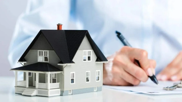 Persona firmando contrato hipotecario con maqueta de casa en primer plano, relacionado con caixa galicia irph y condiciones de préstamos hipotecarios. Metadescripción: Imagen de firma de hipoteca y maqueta de casa, ideal para contenidos sobre caixa galicia irph, reclamaciones, cláusulas abusivas, IRPH vs Euríbor y sentencias.