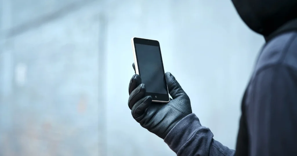 Persona con guantes negros sosteniendo un smartphone, representando un fraude digital vinculado a un sistema Ponzi.