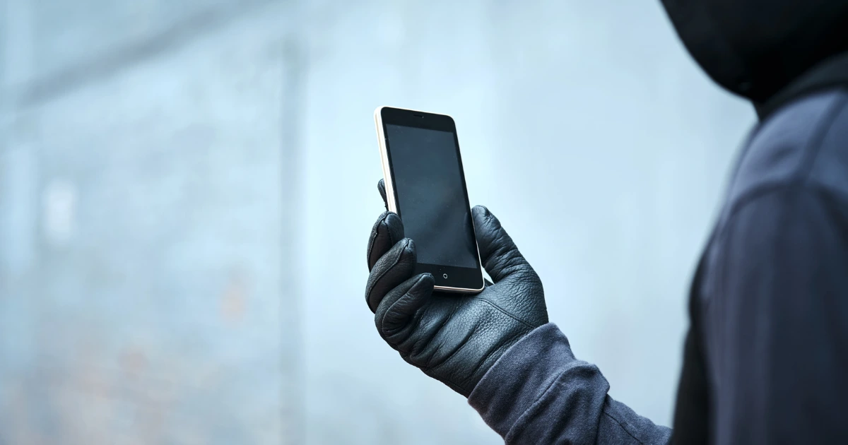 Persona con guantes negros sosteniendo un smartphone, representando un fraude digital vinculado a un sistema Ponzi.