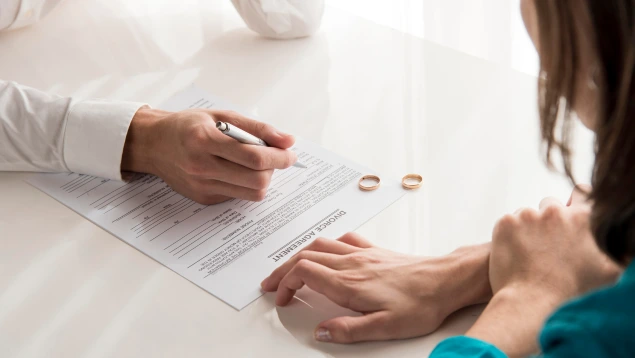 Pareja firmando un acuerdo de divorcio con hipoteca conjunta sobre la mesa junto a dos anillos de matrimonio.