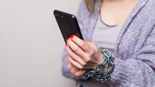 Persona atrapada con cadenas mientras sostiene un móvil, simbolizando una estafa inversión digital.