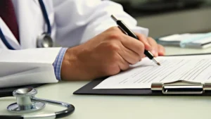 Médico rellenando un formulario sobre un seguro de responsabilidad civil para médicos, con un estetoscopio sobre la mesa.
