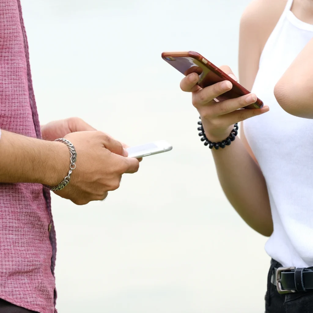 Dos personas sosteniendo sus teléfonos móviles, ilustrando la diferencia entre smishing y phishing, los principales tipos de fraudes digitales y ataques por mensajes falsos.