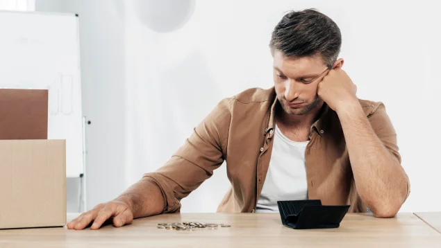 Hombre desempleado mirando su cartera vacía sobre una mesa, representando la búsqueda de préstamos para desempleados en España y las dificultades financieras que pueden resolverse mediante la Ley de Segunda Oportunidad.
