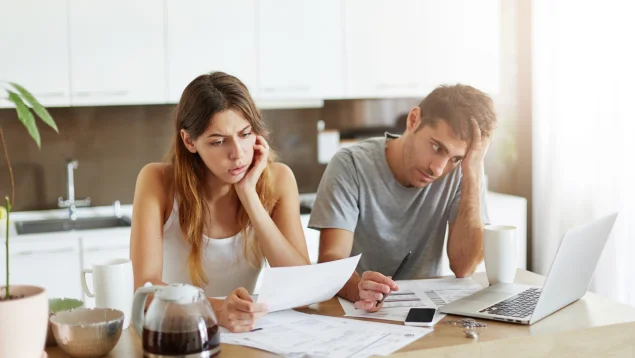 Pareja revisando facturas preocupada en su cocina mientras busca préstamos rápidos Moneyman o minicréditos online para conseguir dinero urgente, reflejando el uso de créditos sin nómina y la posible aplicación de la Ley de Segunda Oportunidad en casos de endeudamiento.