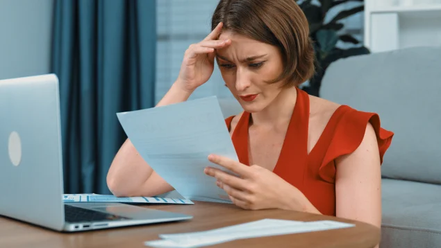 Mujer preocupada revisando documentos frente al ordenador mientras consulta si tiene deudas pendientes. La imagen representa la situación de quienes buscan dónde consultar si tengo deudas con bancos, financieras, Hacienda, Seguridad Social u otros acreedores, y cómo los abogados de Asoban Abogados pueden ayudarles a regularizar su situación económica.