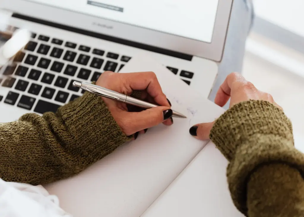 Persona redactando una reclamación por estafa tras sufrir un fraude online, con un ordenador portátil y una libreta sobre la mesa.