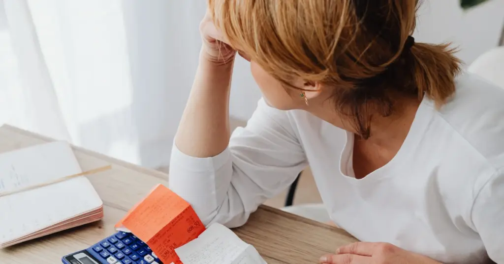 Mujer con expresión de estrés financiero revisando facturas y una calculadora, ilustrando el contexto de las últimas sobre la Ley de segunda oportunidad noticias respecto a la exoneración de deudas.