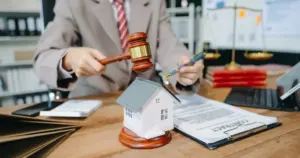 Abogado en despacho jurídico señalando un contrato hipotecario junto a una maqueta de una vivienda para identificar cláusulas abusivas en la ejecución hipotecaria y paralizar el embargo.