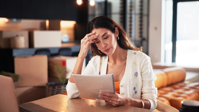 Mujer con expresión de preocupación revisando documentos contables en una oficina con cajas de mudanza, representando una situación de pérdida económica o lucro cesante empresarial.