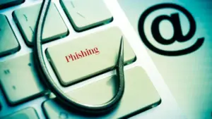 Un anzuelo de pesca sobre un teclado con la palabra "Phishing" y el símbolo de arroba, representando un phishing scam bancario que Asoban Abogados ayuda a combatir.