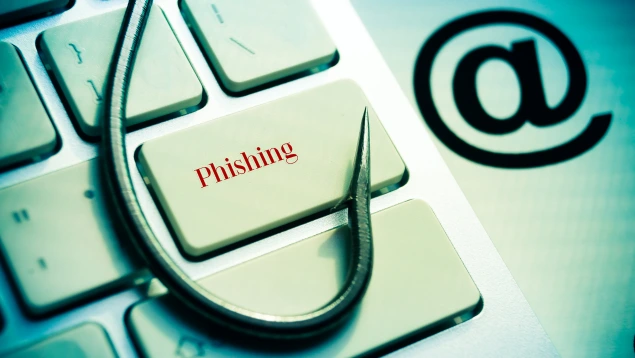 Un anzuelo de pesca sobre un teclado con la palabra "Phishing" y el símbolo de arroba, representando un phishing scam bancario que Asoban Abogados ayuda a combatir.