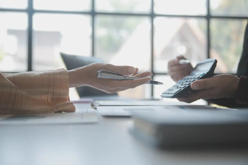 Dos personas en una mesa con luz natural revisando documentos impresos y usando una calculadora para analizar qué es un procedimiento monitorio.